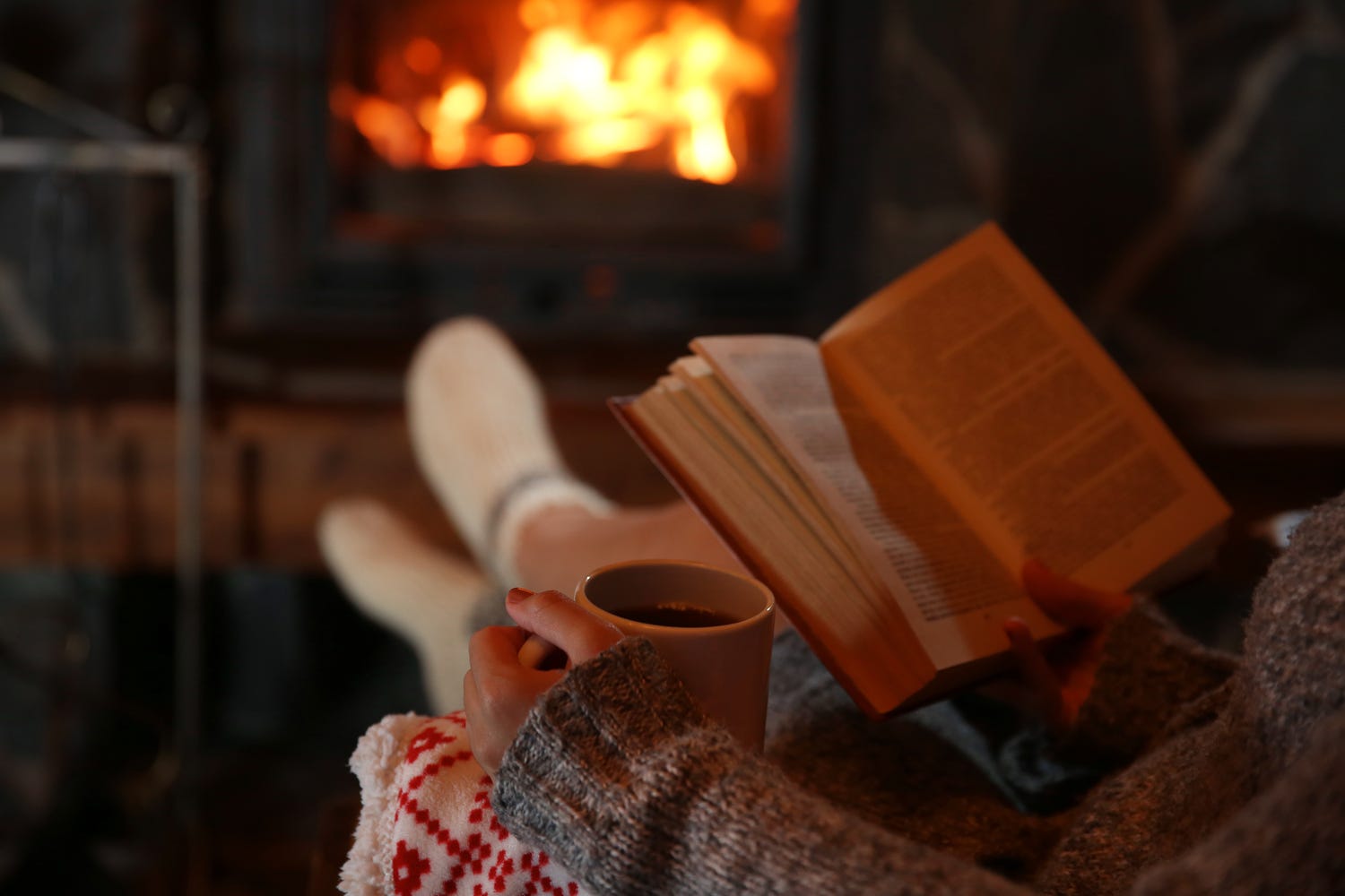 Chica leyendo frente a la chimenea con café